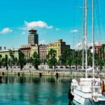 A scenic view of Barcelona harbor with boats and colorful buildings under a clear sky.