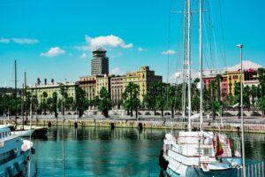 A scenic view of Barcelona harbor with boats and colorful buildings under a clear sky.